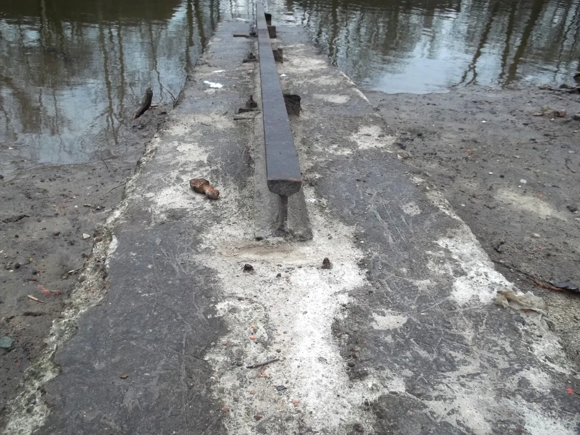 Zbliżenie na zniszczony, skorodowany tor pochylni stoczniowej osadzony w spękanym betonie nad brzegiem kanału w Porcie Czerniakowskim przed rozpoczęciem renowacji przez PBW.